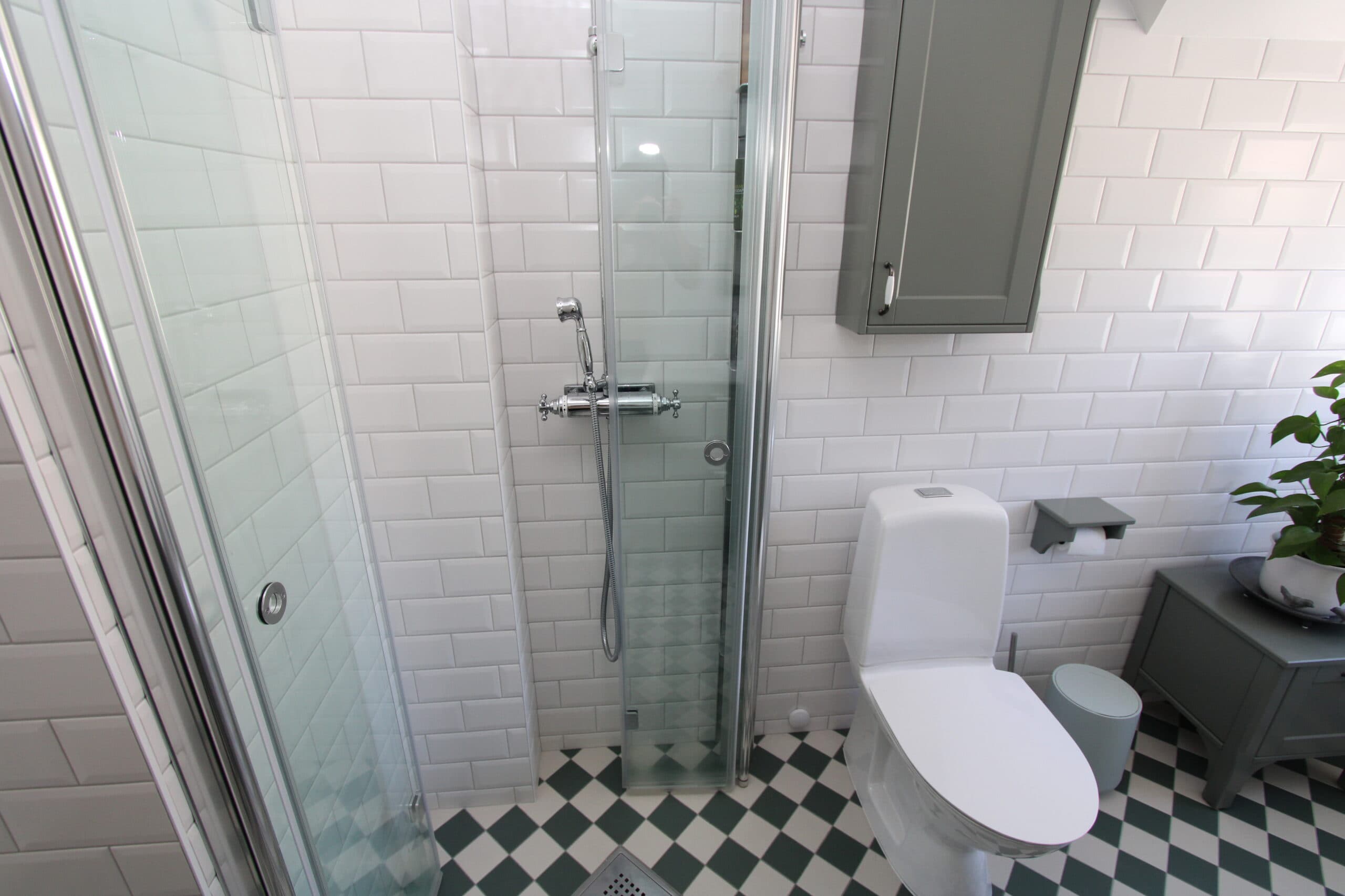 Fräscht badrum med ljusa ytskikt, rund spegel ovanför handfatet och dusch med glasvägg