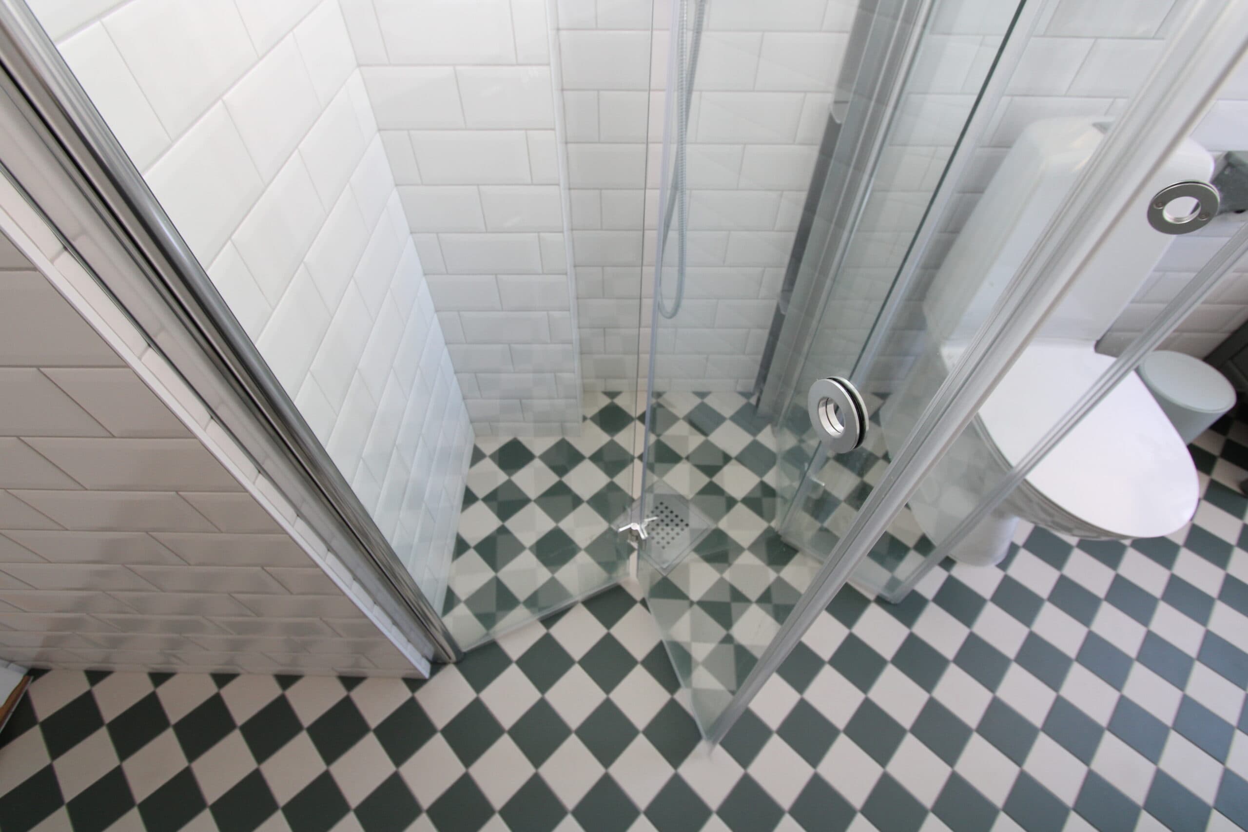 Ljust badrum med stora vita kakelplattor, spegelskåp och dusch med infällbar glasvägg